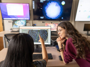 Students Erin Cusson and Niko Kopparapu confer in front of an array of monitors with astronomy data.