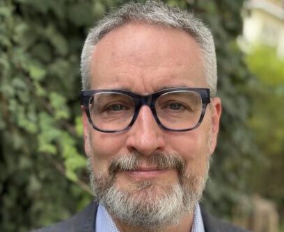 A photo of Scott wearing glasses with foliage behind.