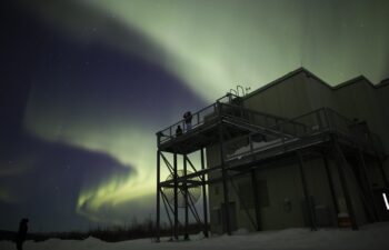 Two students observe aurora borealis arcs above observation facilities at Poker Flat Research Range.